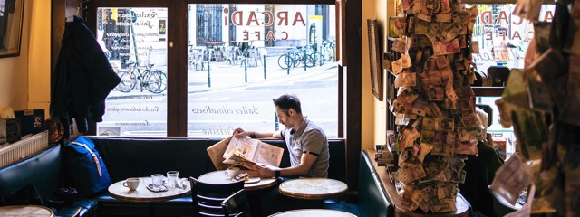 Man leest een krant in een café met zicht op de straat en fietsen buiten.
