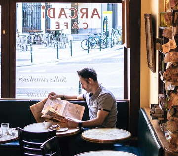Man leest een krant in een café met zicht op de straat en fietsen buiten.