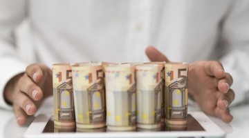 Des mains d'une personne qui rangent des billets de cinq euros sur une tablette.