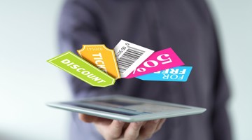 Une main tient une tablette sur laquelle flottent des étiquettes colorées de réduction et de tickets avec des mots comme réduction, ticket et 500.