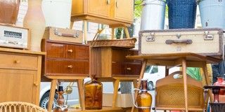 Une pile de meubles et d'accessoires vintage, comprenant une armoire en bois, une valise, un panier et des bouteilles en verre, sur un marché.
