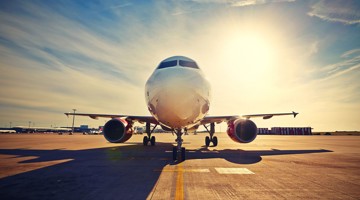 Un avion est stationné sur un aéroport avec le soleil qui brille intensément en arrière-plan.