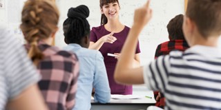 Une enseignante donne cours à une classe d'élèves, certains levant la main pour poser des questions.
