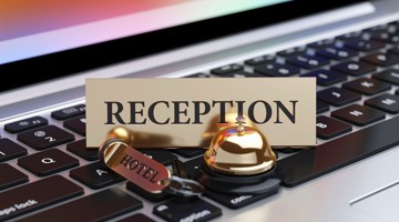 Une cloche d'hôtel en or sur un clavier d'ordinateur portable avec le mot RÉCEPTION en grandes lettres.