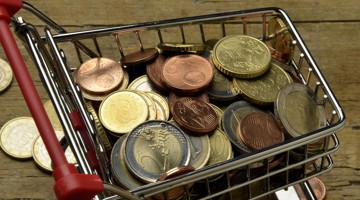 Un chariot de courses rempli de différentes pièces de monnaie sur une surface en bois.
