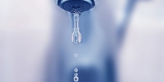 Une goutte d'eau tombe d'un robinet, avec plusieurs petites gouttes en dessous.