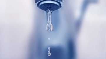 Une goutte d'eau tombe d'un robinet, avec plusieurs petites gouttes en dessous.