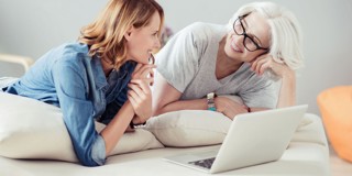 Deux personnes assises sur un lit avec un ordinateur portable, plongées dans une conversation.
