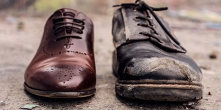 Deux paires de chaussures côte à côte : l'une est une chaussure en cuir marron, brillante et neuve, et l'autre est une chaussure en cuir noir usée, avec des déchirures et de la saleté.