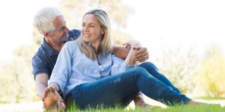 Une femme et un homme sont assis ensemble sur une pelouse, s'enlaçant et se détendant au soleil.
