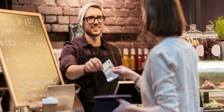 Un barista remet un reçu à un client au comptoir d'un café, avec un tableau noir en arrière-plan.