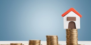Een klein modellenhuisje met een rood dak op een stapel munten, dat symboliseert dat wonen een financiële investering is.