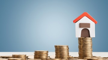 Een klein modellenhuisje met een rood dak op een stapel munten, dat symboliseert dat wonen een financiële investering is.