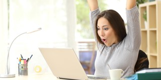 Femme assise derrière un ordinateur portable, affichant une posture détendue avec les bras levés. Sur la table se trouvent une tasse et des fournitures de bureau.