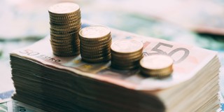 Des piles de pièces empilées sur une liasse de billets en euros, avec les pièces augmentant en hauteur.