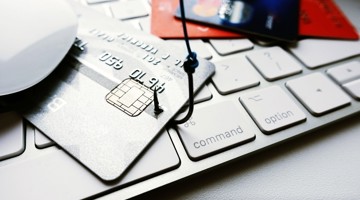 Een zilveren bankpas ligt op een laptoptoetsenbord, omringd door andere kredietkaarten en een computermuis.