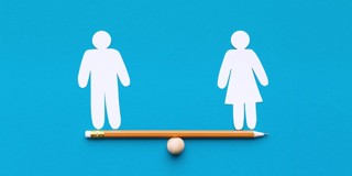Une poutre d'équilibre avec une boule en bois motivée au centre, sur laquelle repose un crayon. Sur le côté gauche, un symbole en papier représentant un homme, et sur le côté droit, un symbole en papier représentant une femme.