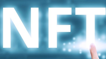 Un doigt pointe vers les grandes lettres NFT sur un fond bleuté.