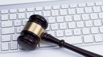 Un marteau de juge repose sur un clavier d'ordinateur, symbolisant la combinaison du droit et de la technologie.