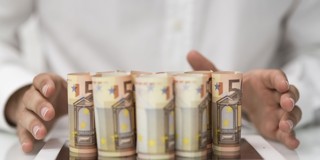 Vijf opgestapelde eurobiljetten met twee handen eromheen.