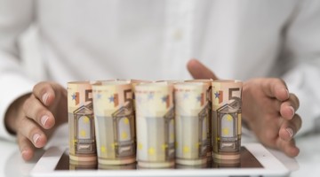 Vijf opgestapelde eurobiljetten met twee handen eromheen.