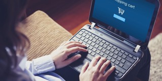Persoon met een laptop die een scherm toont met een online winkelwagentje en een knop om verder te gaan.