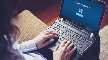 Persoon met een laptop die een scherm toont met een online winkelwagentje en een knop om verder te gaan.