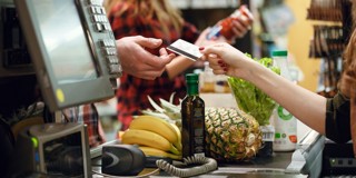 Een klant overhandigt een betaalpas aan de kassamedewerker in een supermarkt, omringd door verschillende boodschappen zoals fruit en groenten.