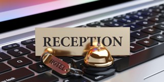 Een gouden receptiebell met een hotellabel ligt op een laptoptoetsenbord, met het woord 'RECEPTION' duidelijk zichtbaar in het midden.
