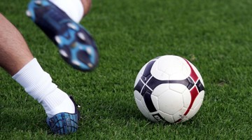 Een voet van een speler raakt een zwart-wit gestreepte bal op het gras.