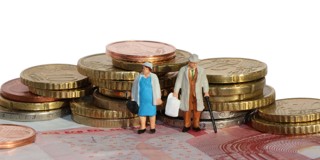 Twee kleine figuren van een ouder echtpaar staan tussen stapels munten op een bed van briefgeld.