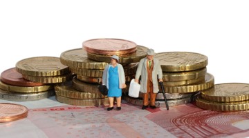 Twee kleine figuren van een ouder echtpaar staan tussen stapels munten op een bed van briefgeld.