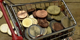 Een winkelwagentje gevuld met verschillende euromunten op een houten ondergrond.