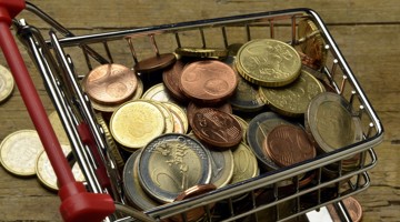 Een winkelwagentje gevuld met verschillende euromunten op een houten ondergrond.
