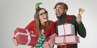 Vrolijke mensen in kerstoutfits, omringd door versierde cadeaus en een kerstbel.