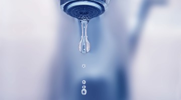 Een druppelende waterkraan met naast elkaar hangende druppels.