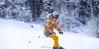 Skiër in een kleurrijke winteroutfit glijdt over een besneeuwde helling, omringd door bomen.