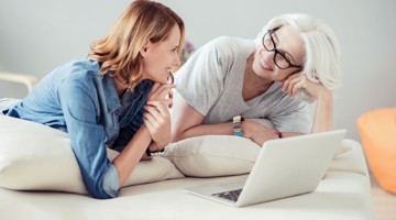 Twee mensen zitten op een bed, leunend op kussens terwijl ze naar een laptop kijken.