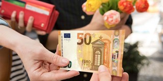 Een hand reikt een vijftig euro biljet aan een andere hand die een boeket bloemen vasthoudt.
