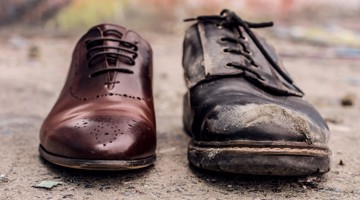 Een rechterbruine leren schoen naast een linkervieze, zwarte leren schoen met slijtage.