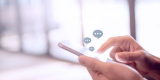 Hand die een smartphone vasthoudt met boven het scherm tekstballonnen die berichten weergeven.