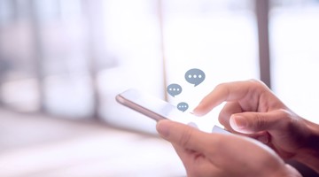 Hand die een smartphone vasthoudt met boven het scherm tekstballonnen die berichten weergeven.