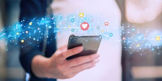 Een persoon houdt een smartphone vast, omringd door sociale media-iconen en hartjes die digitale interactie symboliseren.