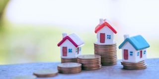 Miniatuurhuisjes op stapels munten, wat vastgoed en financiële groei symboliseert.