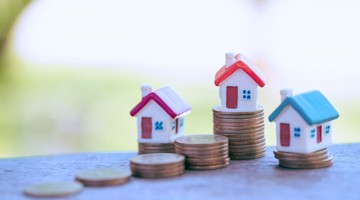 Miniatuurhuisjes op stapels munten, wat vastgoed en financiële groei symboliseert.