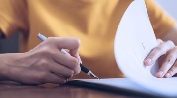Een hand houdt een pen vast en bladert door een stapel papieren.