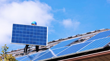Een technicus die zonnepanelen op een woonhuisdak installeert.