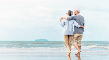 Een ouder echtpaar wandelt langs het strand en geniet van elkaars gezelschap.