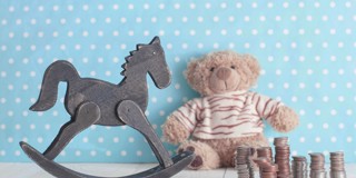 Un cheval à bascule en bois à côté d'un ours en peluche et d'une pile de pièces sur un fond bleu clair à pois blancs.