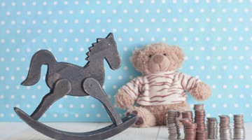 Un cheval à bascule en bois à côté d'un ours en peluche et d'une pile de pièces sur un fond bleu clair à pois blancs.